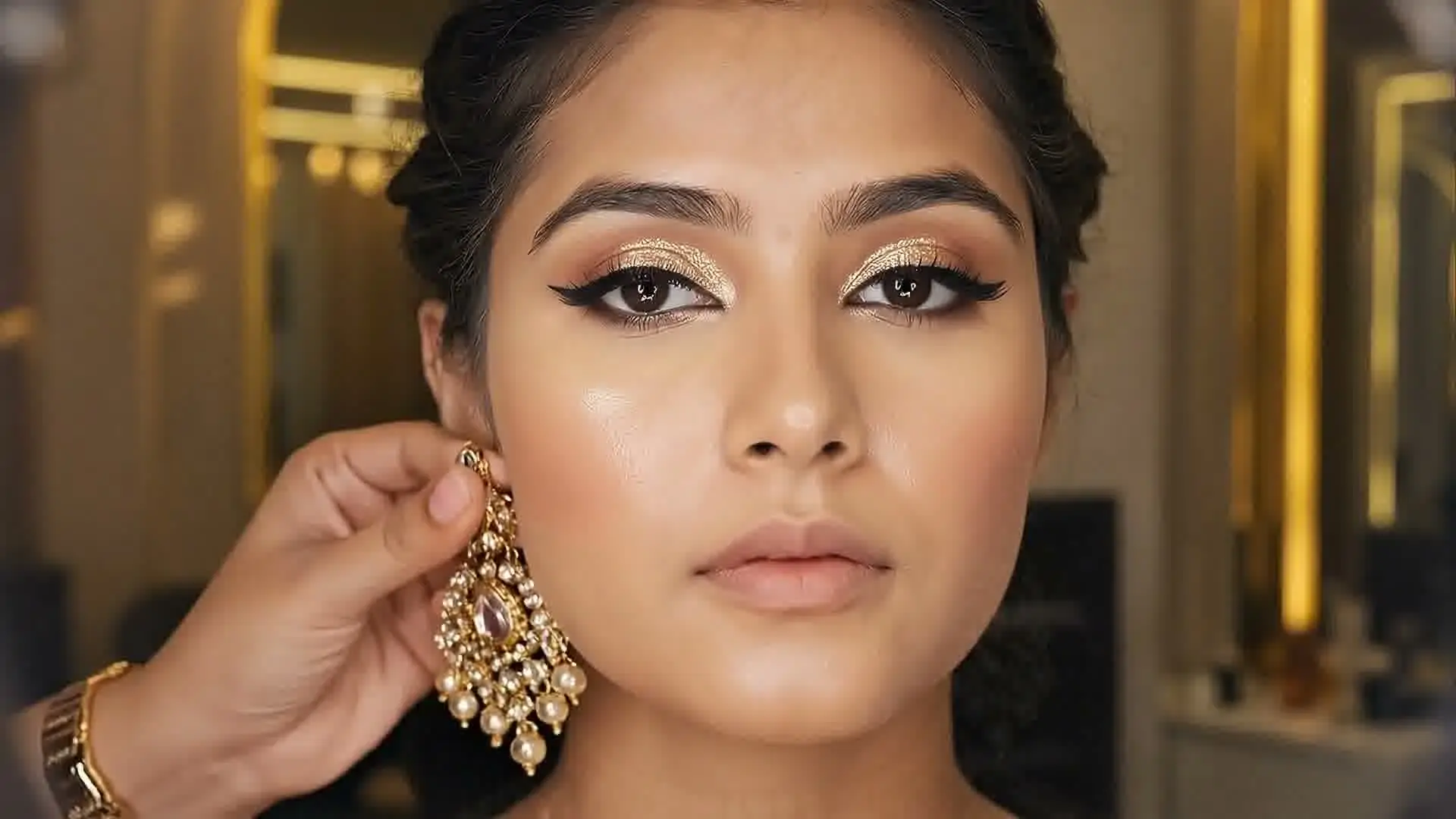 A kundan earring being fastened on a woman's ear during her bridal makeup